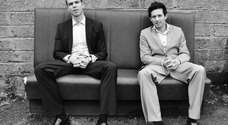 Russell Isabelle and Patrick Cunningham sat on a sofa wearing suits
