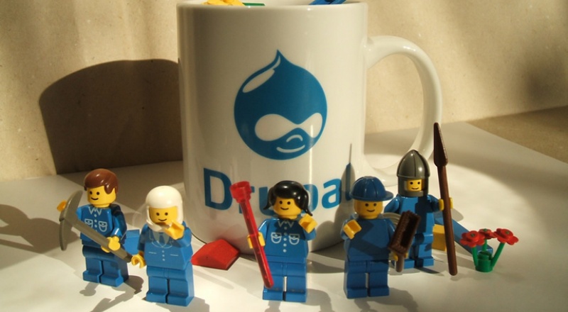 Playmobil figures around a mug with the Drupal logo on it