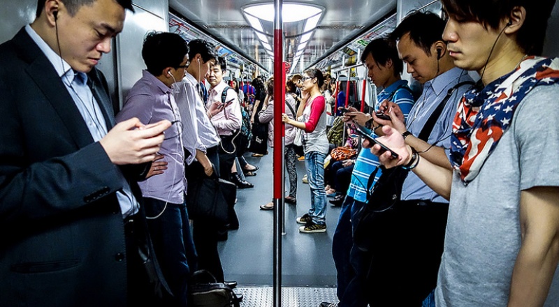 Many people using their phones on a busy tube with headphones in