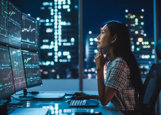 Financial analyst at workstation reviewing data on monitors